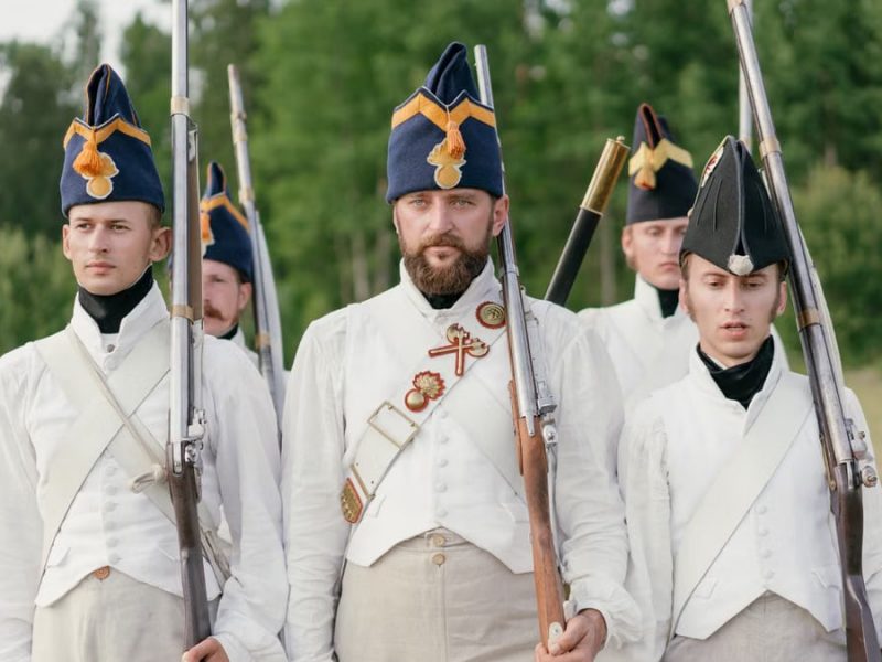 Soldiers marching in historical military uniforms reenact past events outdoors.